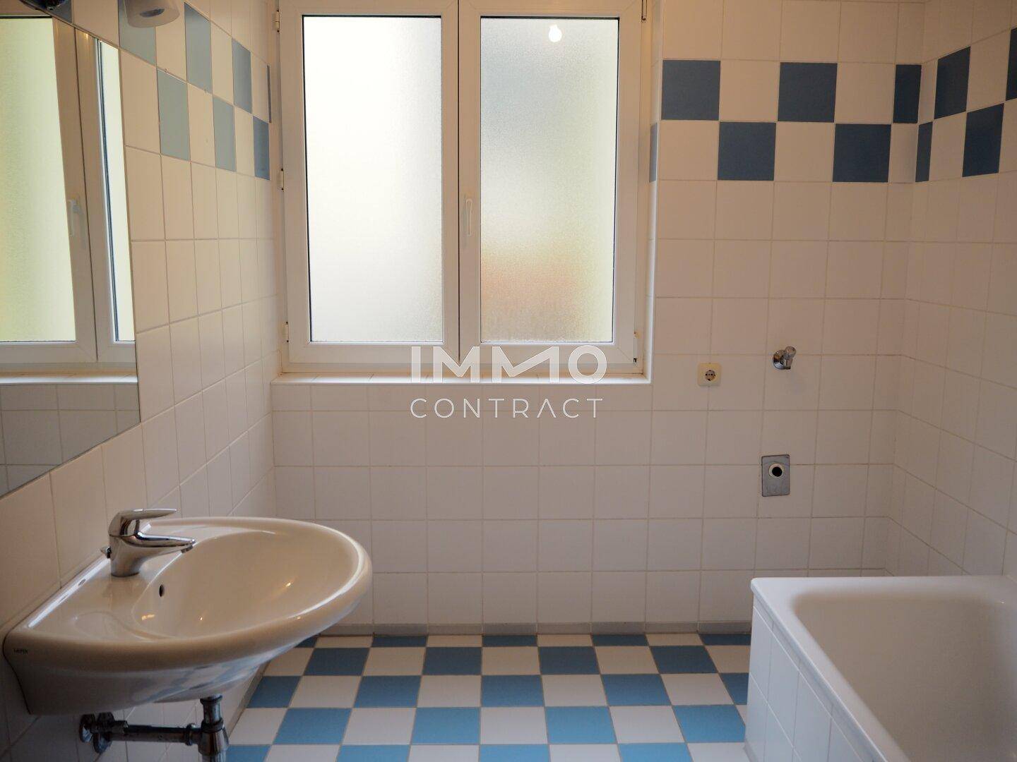 Badezimmer mit weiß-blauen Fliesen, Waschbecken und Badewanne, ausgestattet mit Fenster.