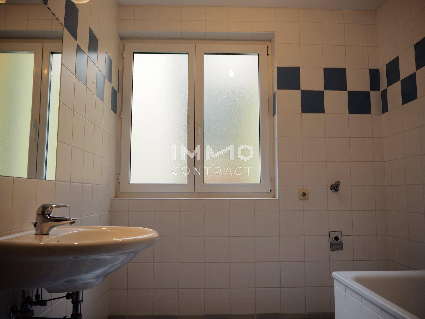 Badezimmer mit weiß-blauen Fliesen, Waschbecken und Badewanne, ausgestattet mit Fenster.