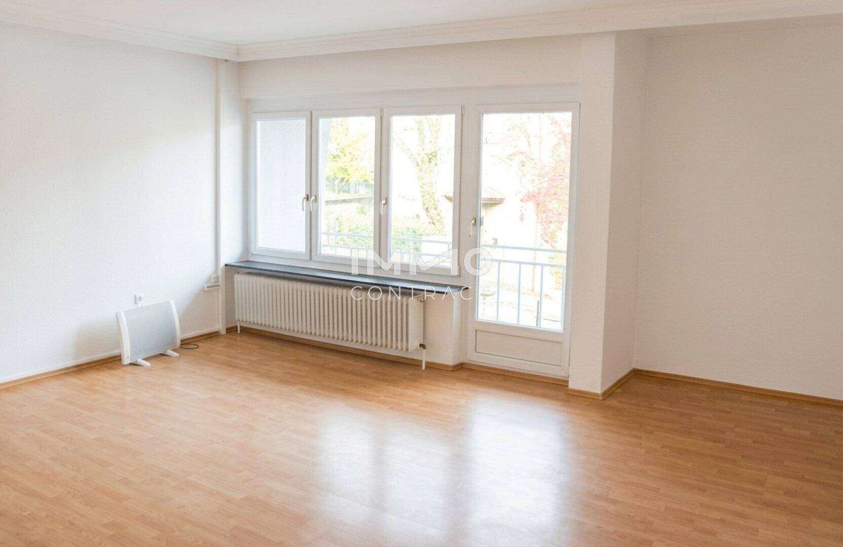 Heller Wohnraum mit Laminatboden, großem Fenster und Zugang zu einem kleinen Balkon.