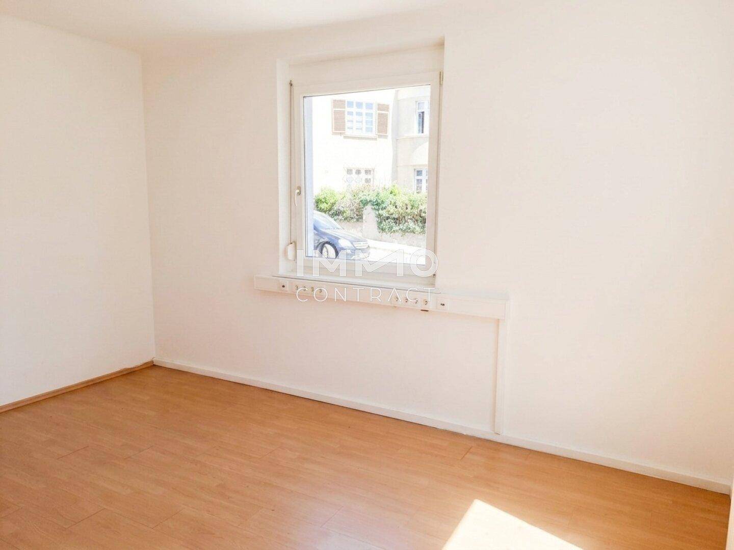 Leerer Raum mit hellem Laminatboden und einem Fenster, das auf die Straße blickt.