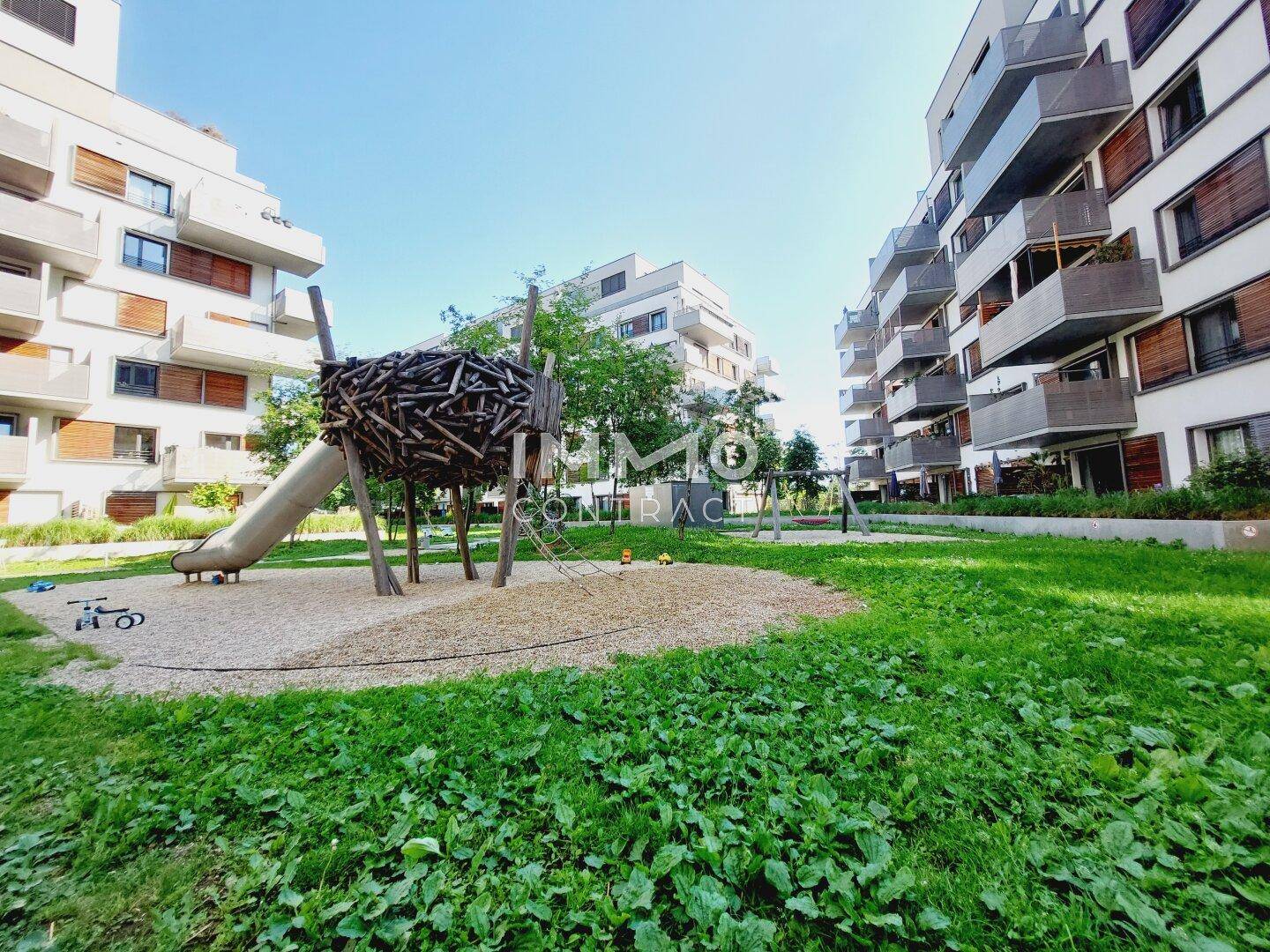 Kinderspielplatz mit Rutsche und Grünflächen innerhalb einer modernen Wohnanlage.
