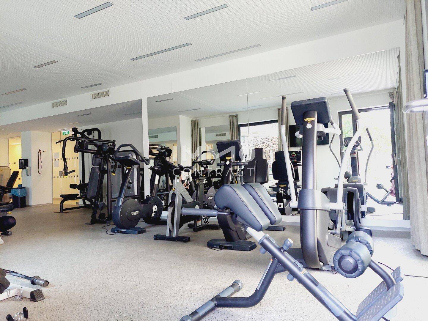 Gut ausgestatteter Fitnessraum mit verschiedenen Trainingsgeräten und großen Spiegeln.