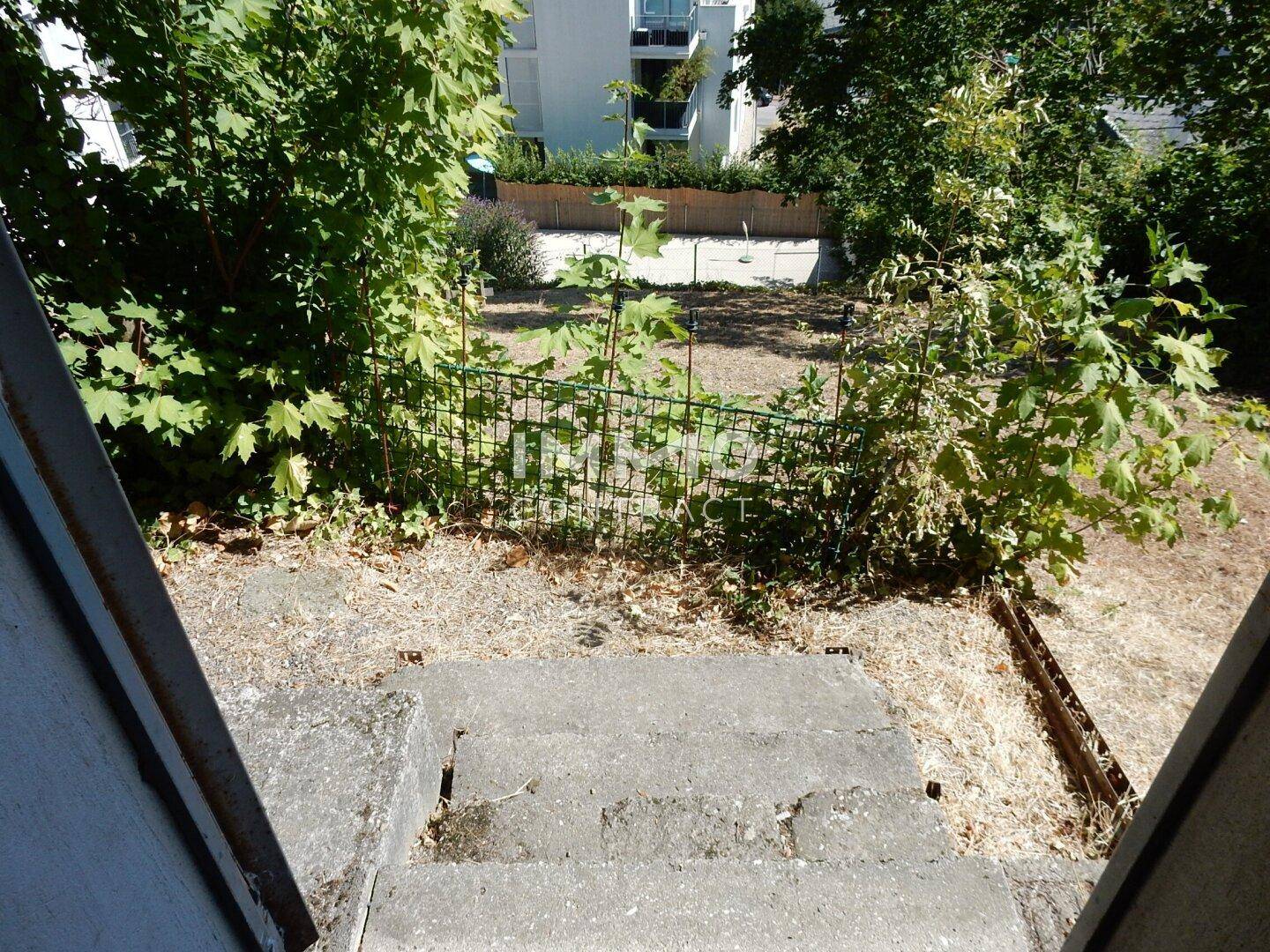 Blick von Betontreppen in einen kleinen, verwilderten Gartenbereich mit umliegenden Gebäuden.
