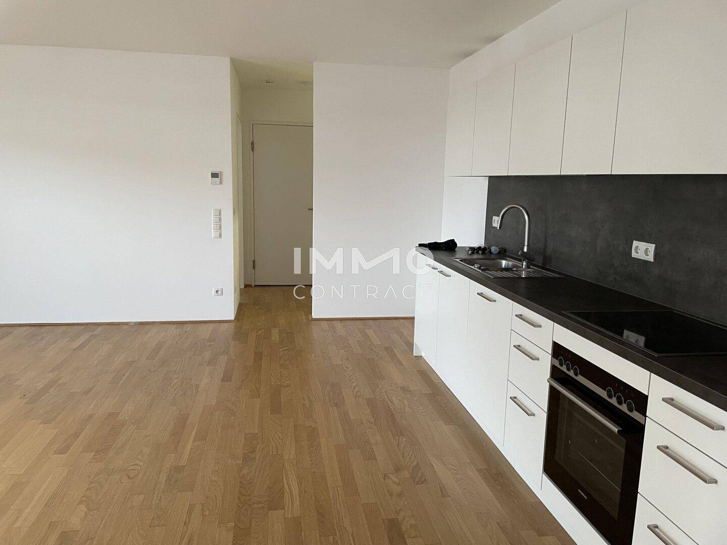 Moderne Einbauküche mit weißen Fronten und dunkler Arbeitsplatte in einem offenen Wohnbereich.
