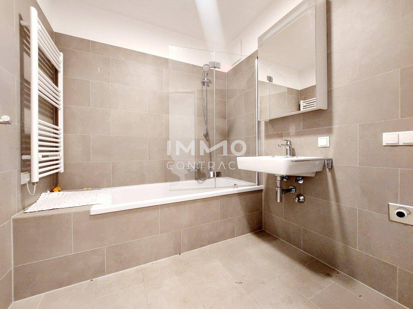 Modernes Badezimmer mit beigefarbenen Fliesen, Badewanne mit Dusche und beheiztem Handtuchhalter.