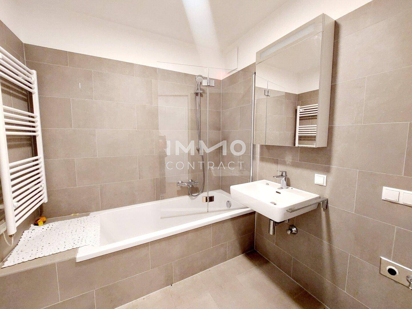 Modernes Badezimmer mit beigefarbenen Fliesen, Badewanne mit Dusche und beheiztem Handtuchhalter.