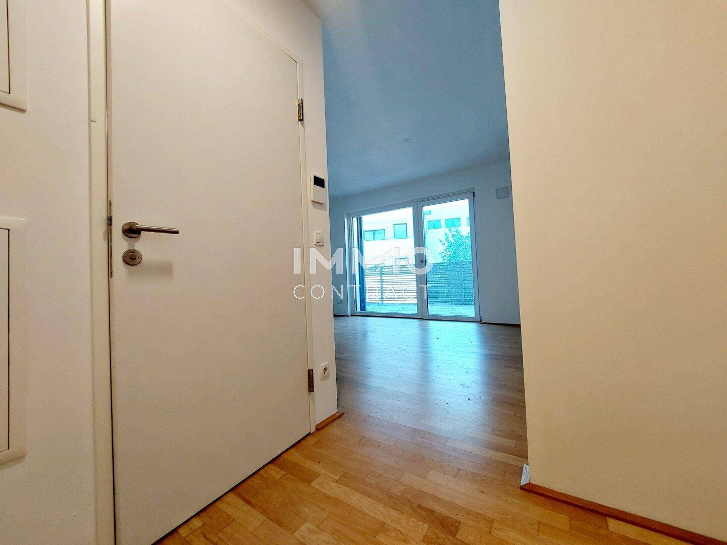 Blick vom Flur in den hellen Wohnbereich mit großen Fenstern und Holzboden.