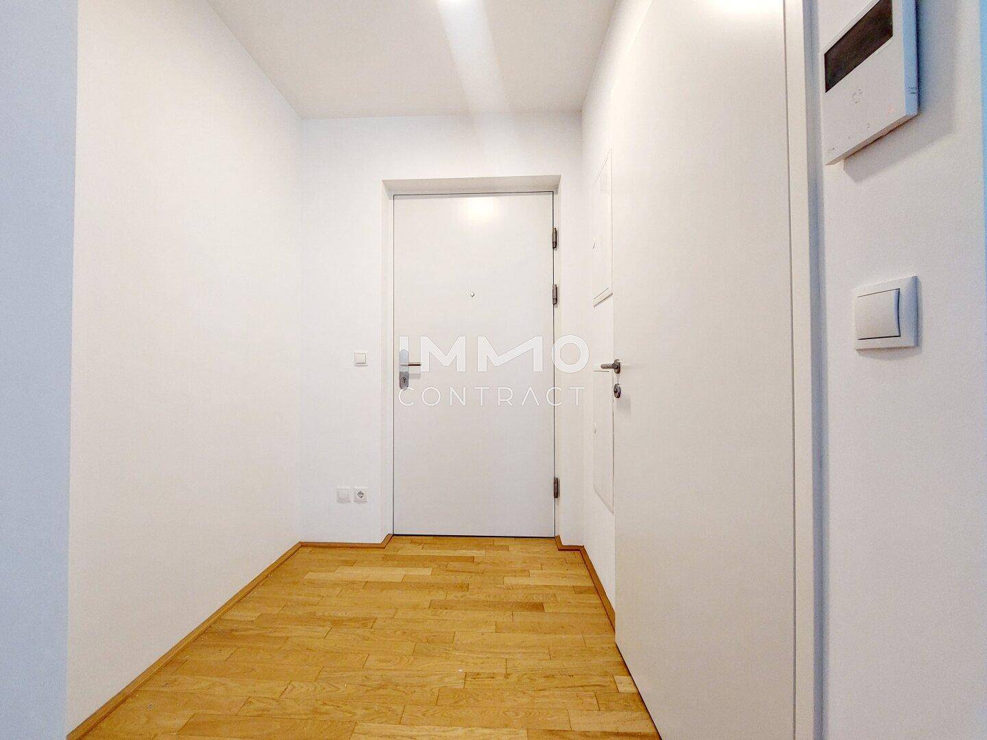 Heller Eingangsbereich mit Holzboden und weißer Eingangstür, der in die Wohnung führt.