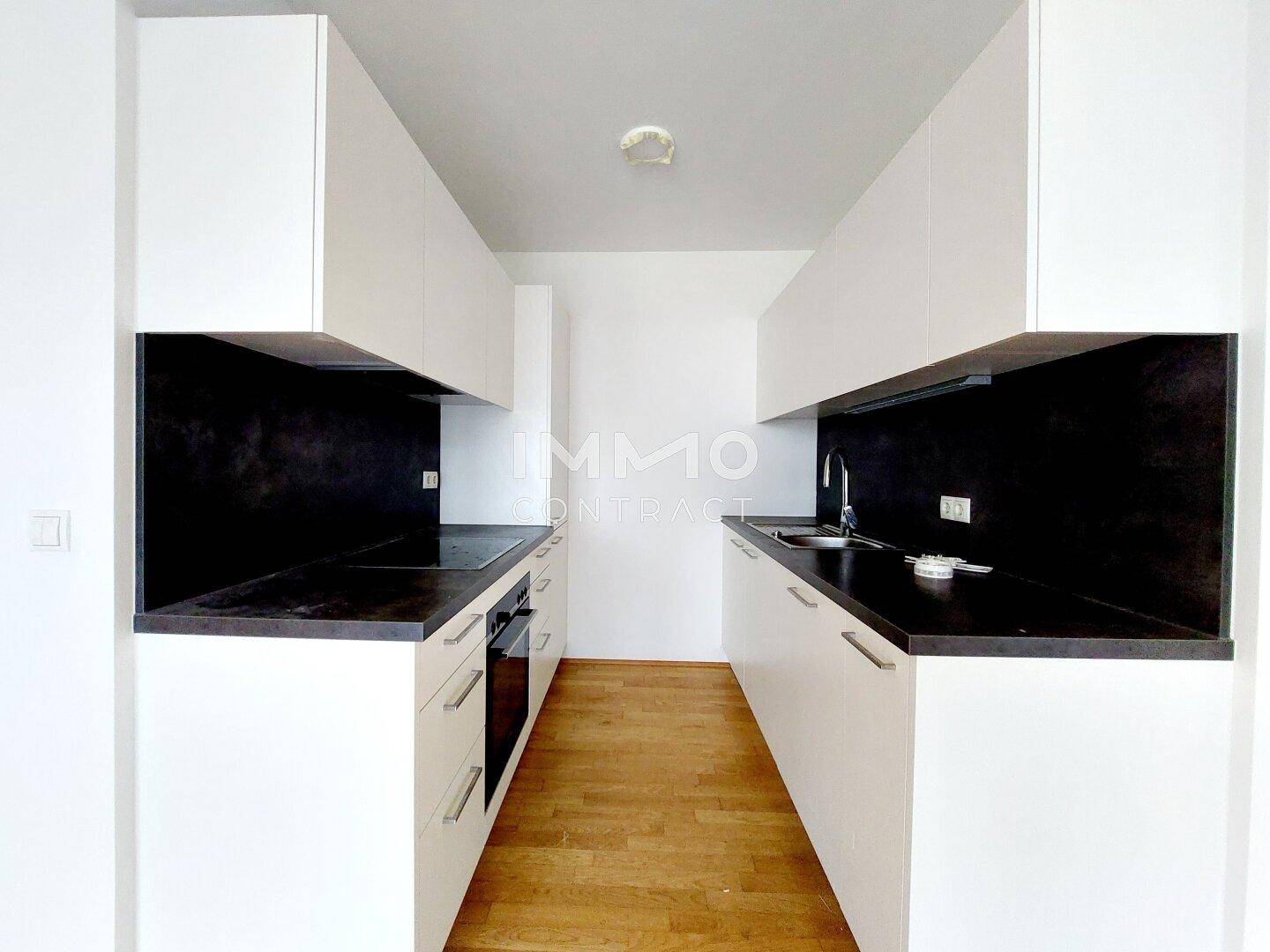 Moderne Einbauküche mit weißen Schränken, dunklen Arbeitsplatten und integrierten Geräten.