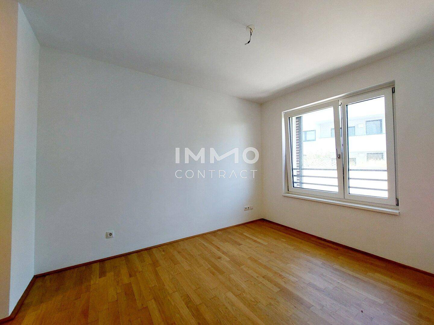 Helles Schlafzimmer mit Holzboden und einem großen Fenster, das viel Tageslicht hereinlässt.