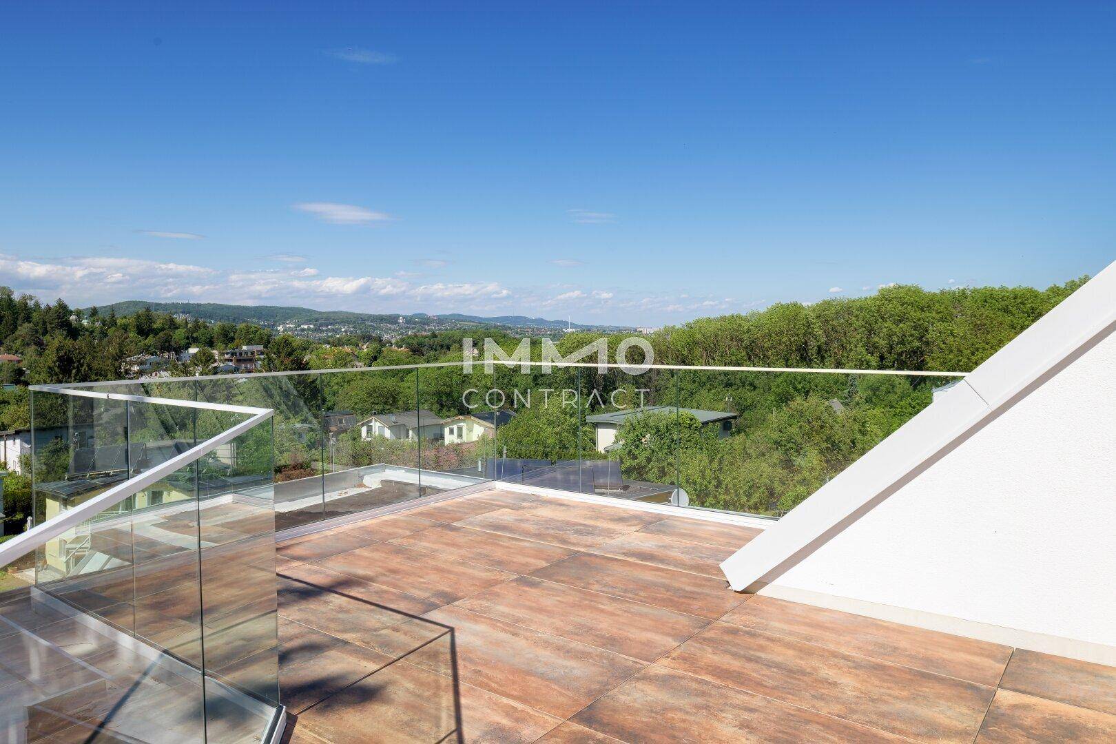 Große Dachterrasse mit Glasgeländer und weitem Blick über die grüne Umgebung und die Stadt.