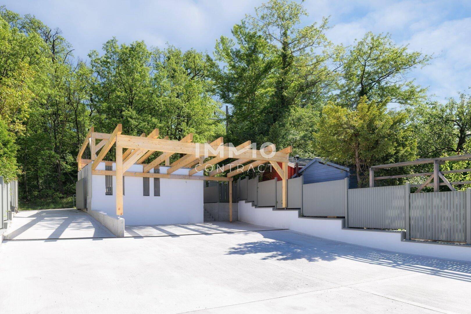 Geräumiger Parkplatz mit Holz-Carport und Zufahrt, umgeben von Bäumen.