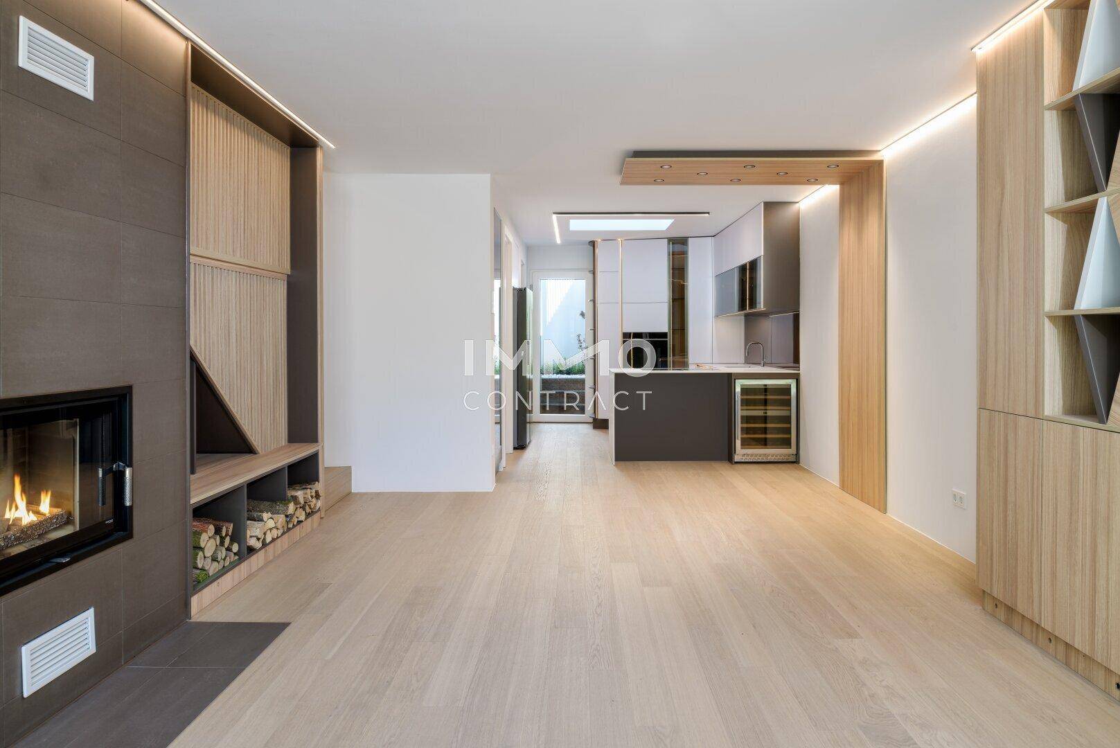 Offener Wohnbereich mit Kamin, Holzboden und Blick auf die moderne Küche im Hintergrund.