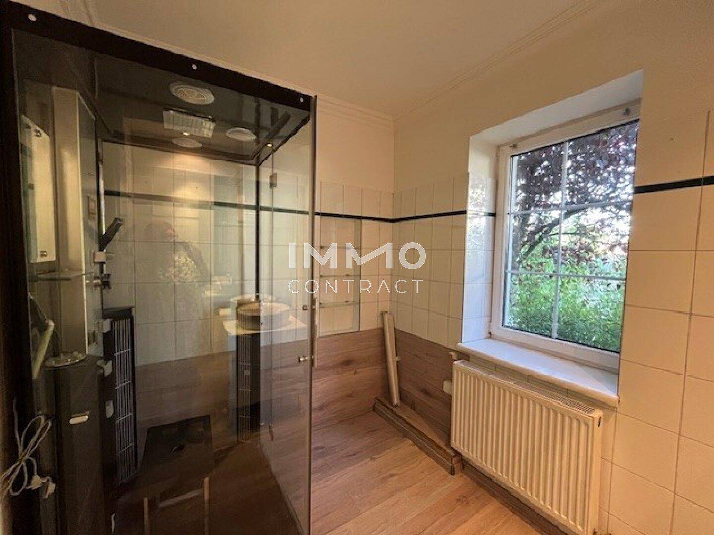 Badezimmer mit Duschkabine, hellen Fliesen und einem Fenster, das Tageslicht hereinlässt.