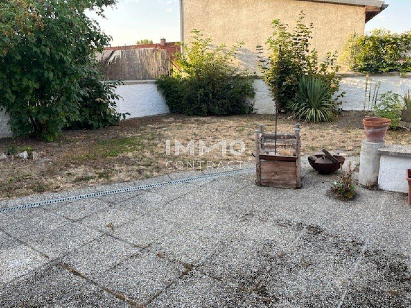 Gepflegter Gartenbereich mit großer Steinterrasse und Rasenfläche unter blauem Himmel.