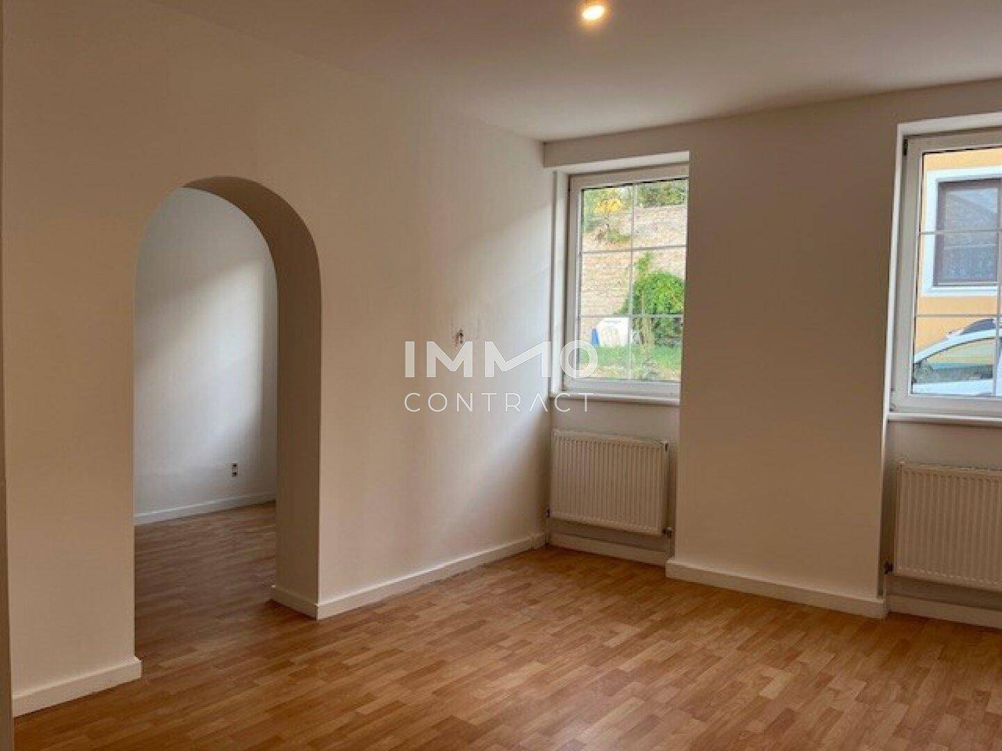 Helles Wohnzimmer mit Holzboden, großen Fenstern und einem eleganten Bogendurchgang.