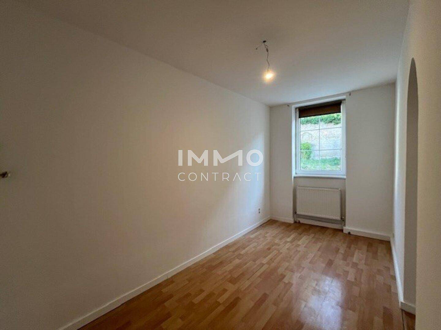 Ruhiges Schlafzimmer mit Holzboden, hellen Wänden und einem Fenster mit Blick ins Grüne.