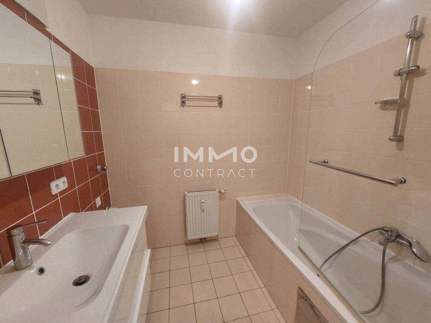 Badezimmer mit Badewanne, Waschbecken und hellen Fliesen an Wänden und Boden.