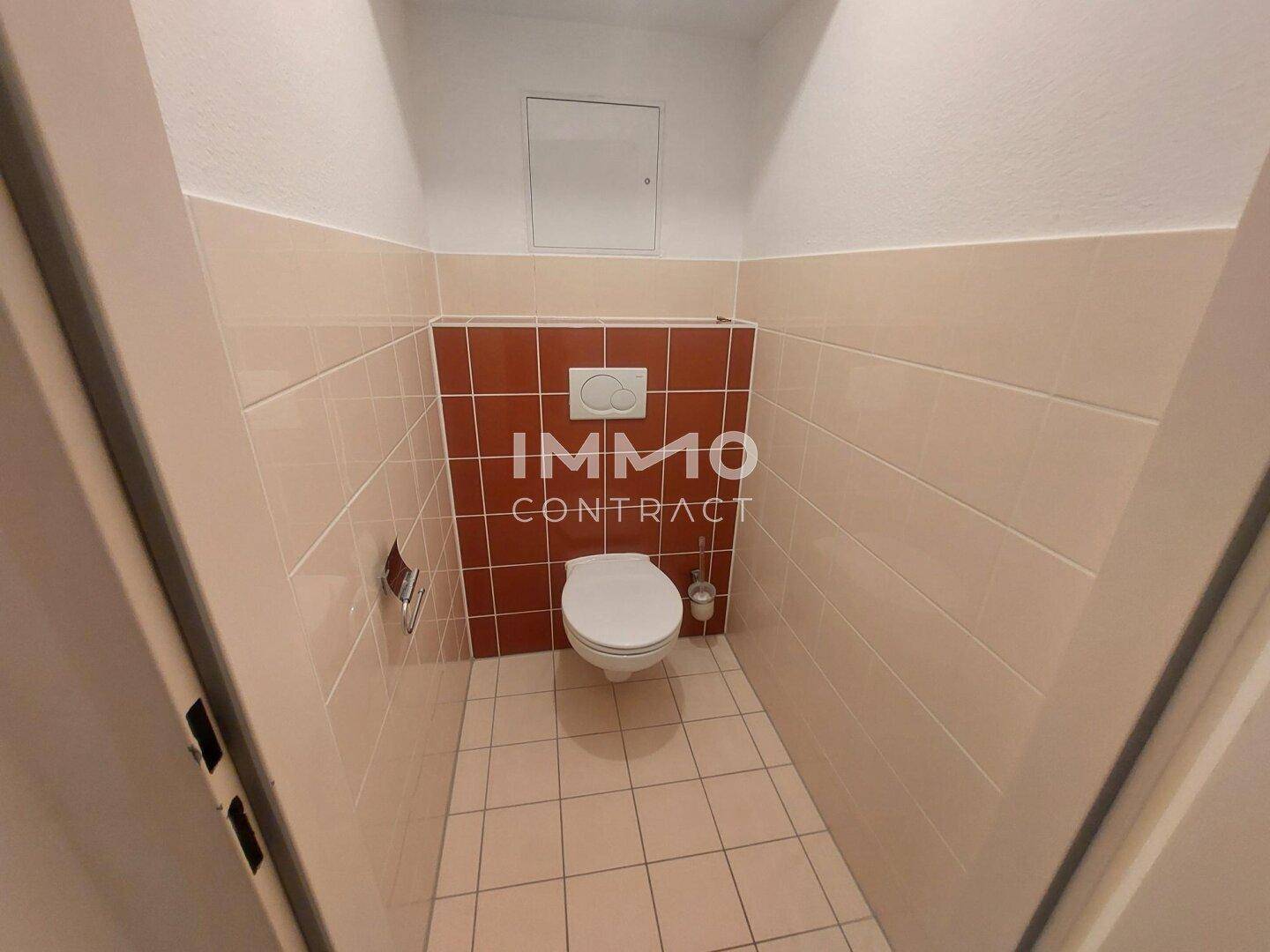 Separate Toilette mit Wand-WC und Fliesen an den Wänden und auf dem Boden.