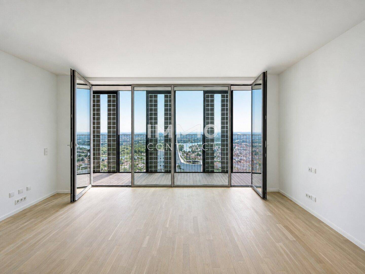 Geräumiger, heller Raum mit Holzboden und einer Fensterfront, die einen weiten Blick über die Stadt freigibt.
