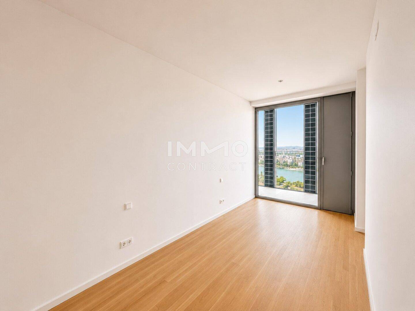 Helles Schlafzimmer mit Holzboden und großem Fenster, das einen weiten Blick auf die Stadt bietet.