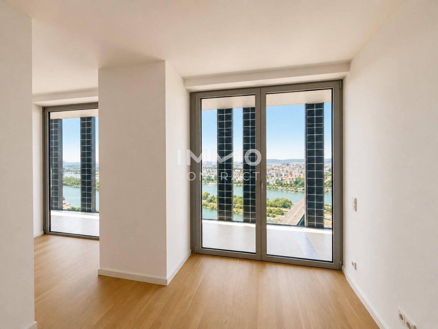 Lichtdurchfluteter Raum mit modernem Holzboden und Panoramafenstern mit Blick auf die Donau und die Stadt.