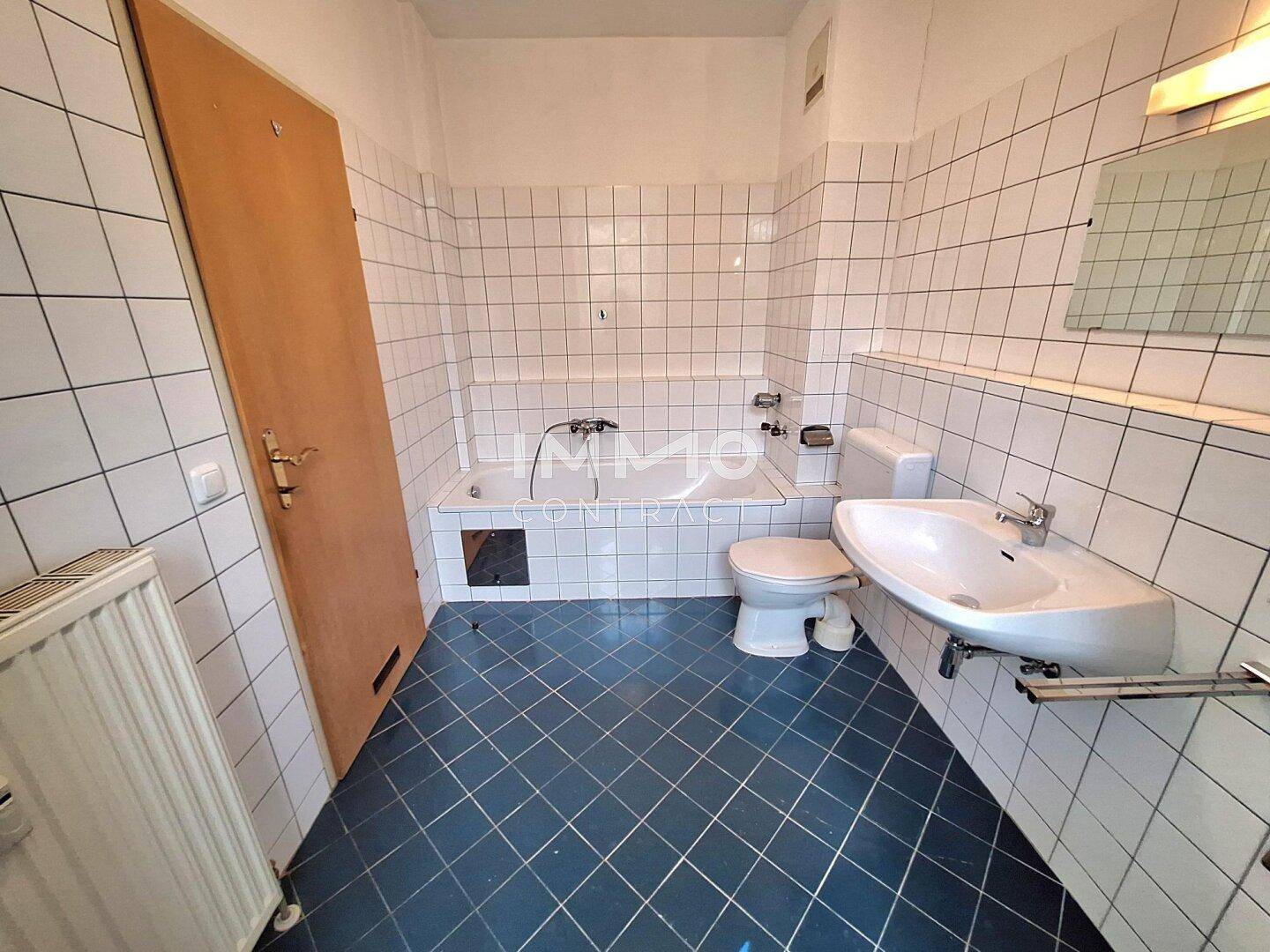 Badezimmer mit Badewanne, WC, Waschbecken, weißen Wandfliesen und blauen Bodenfliesen.