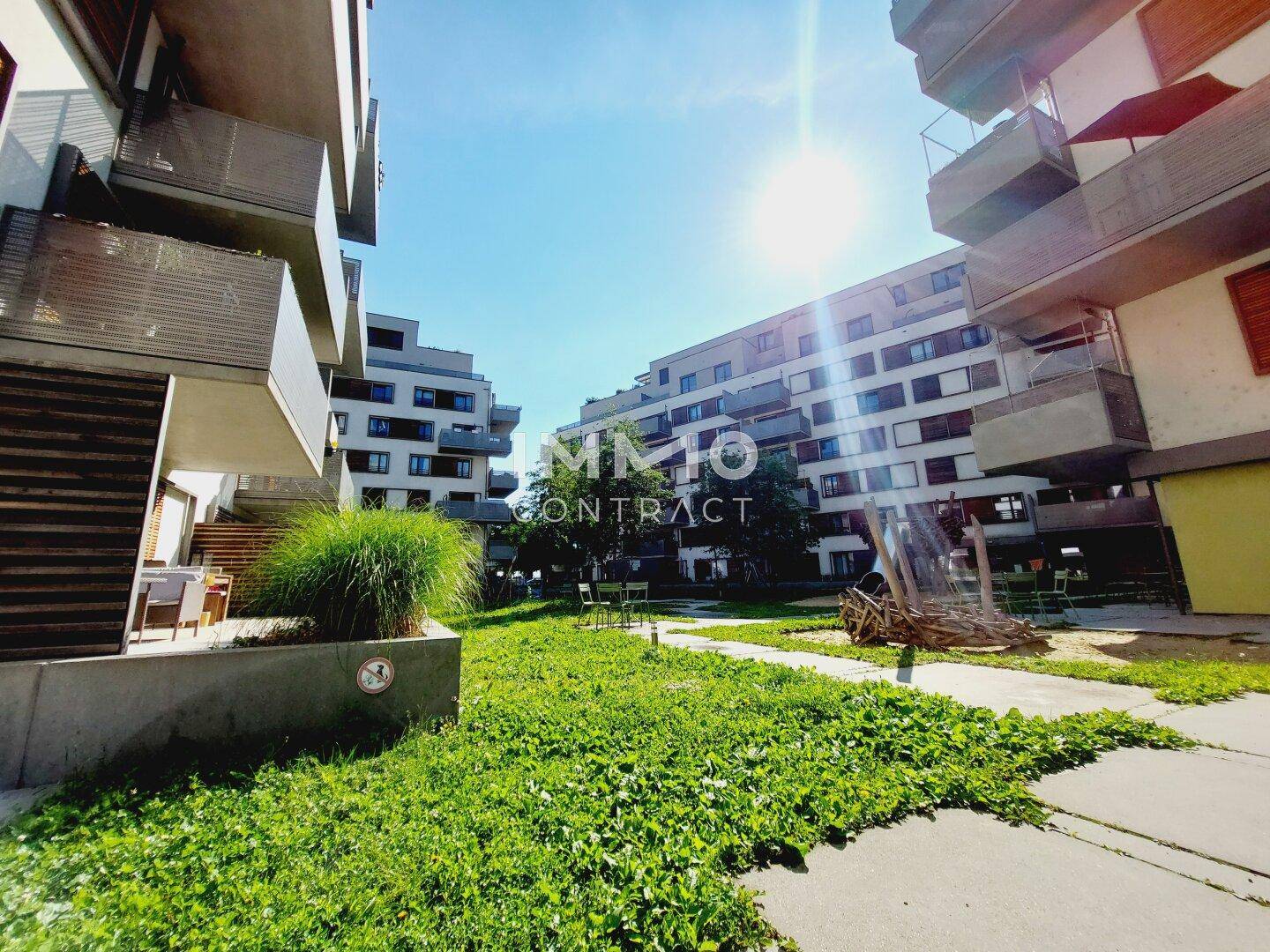 Sonnige Grünfläche im Innenhof der Wohnanlage mit Wegen und modernen Gebäuden im Hintergrund.