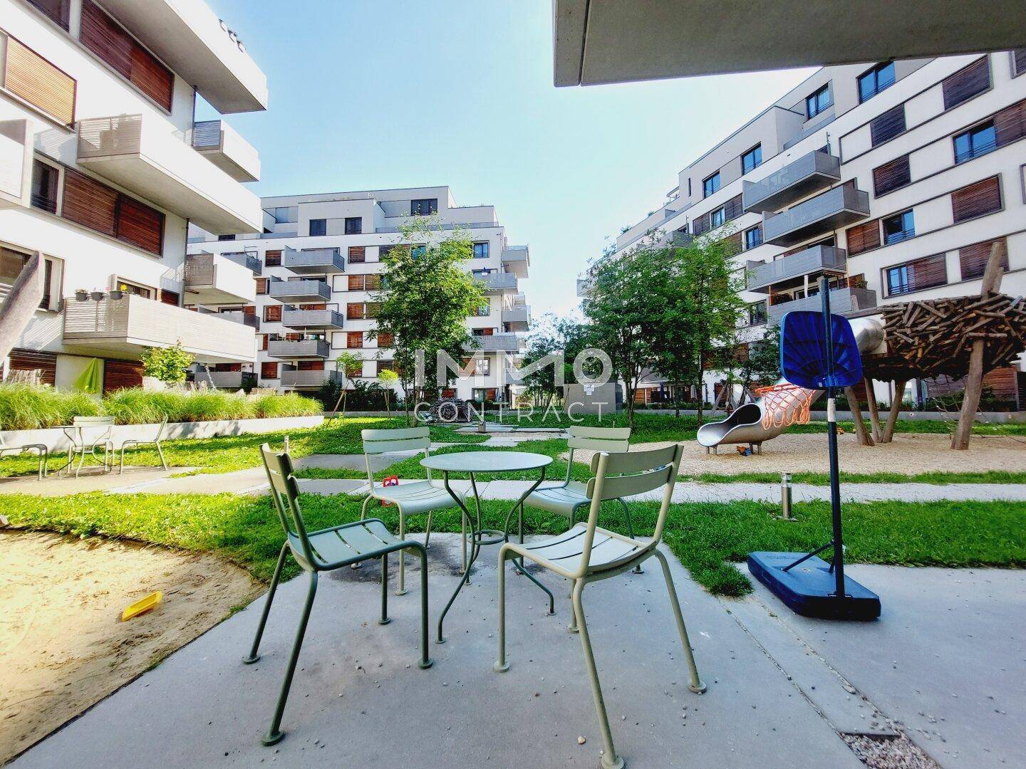 Gemeinschaftlicher Gartenbereich mit Sitzgelegenheiten und Kinderspielplatz in der modernen Wohnanlage.