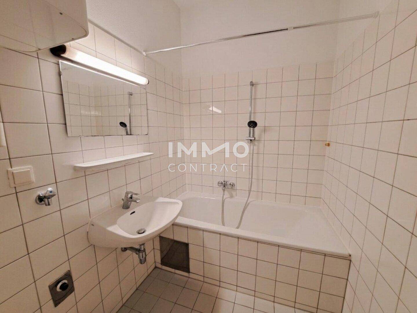 Funktionales Badezimmer mit weißen Fliesen, Badewanne mit Duschfunktion und Einzelwaschbecken.