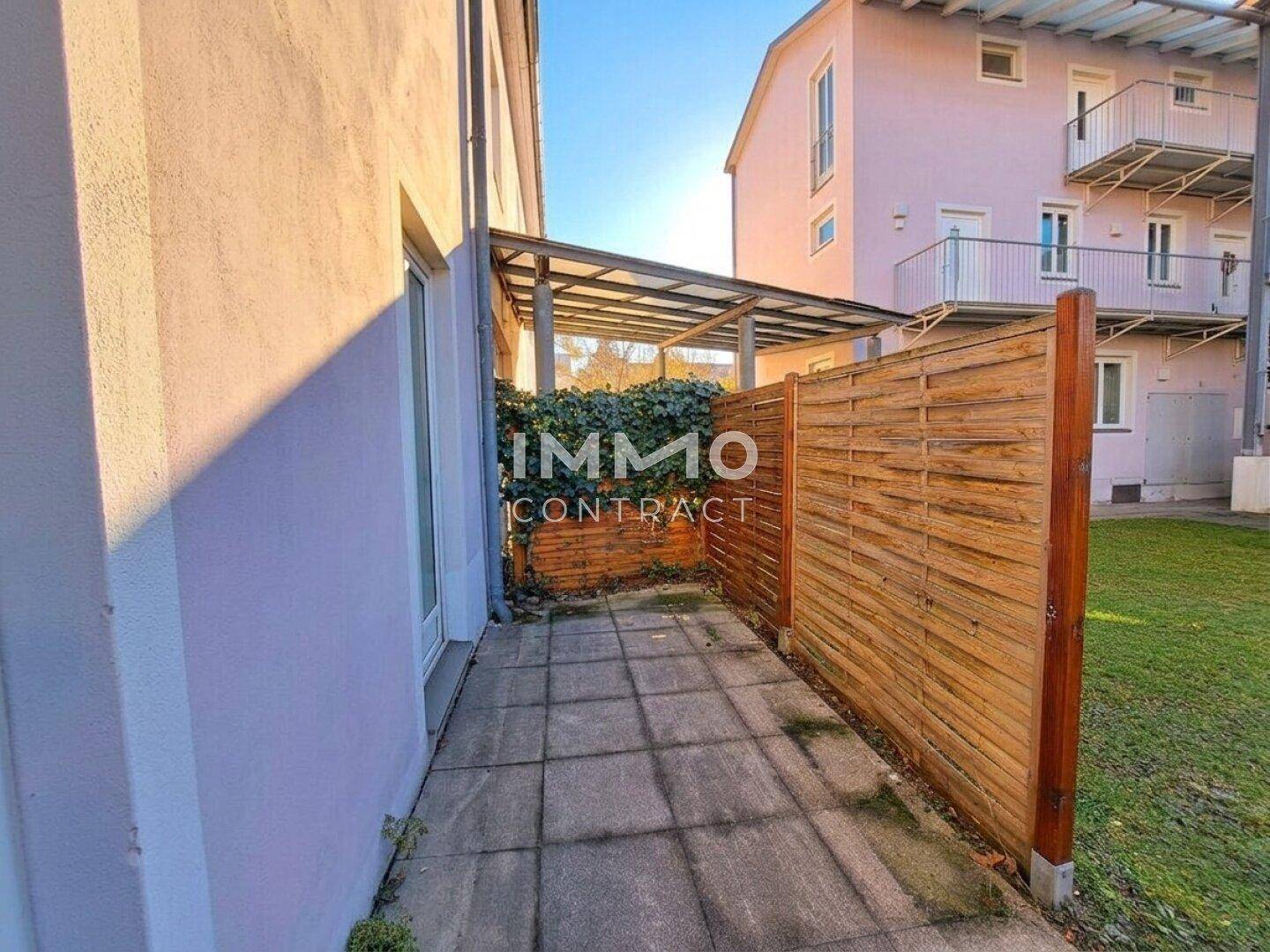 Gepflasterte Terrasse mit Holzzaun, umgeben von Grünflächen und einem überdachten Bereich.