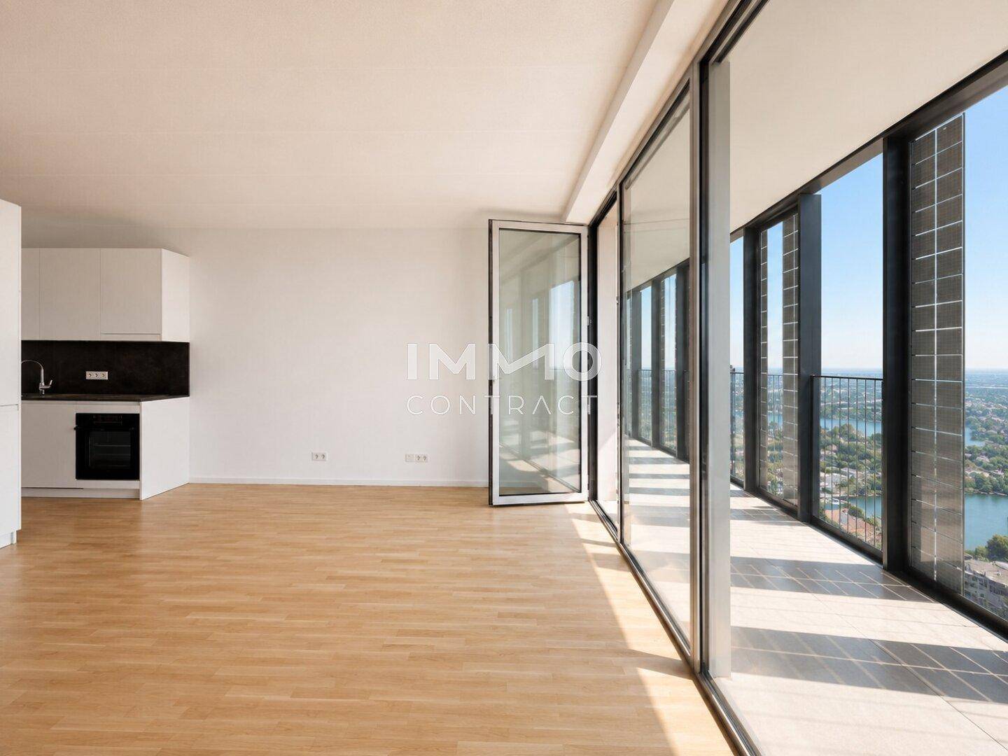 Heller, leerer Wohnraum mit Holzboden, großen Fenstern und Blick auf die Stadt und den Fluss.
