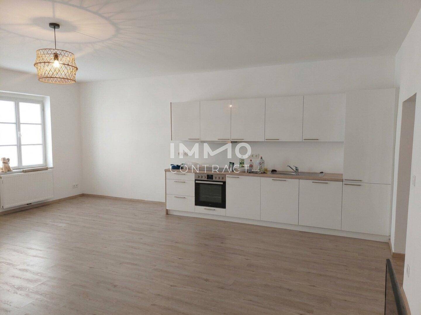 Moderne Einbauküche mit weißen Schränken und Laminatboden in einem hellen Raum.