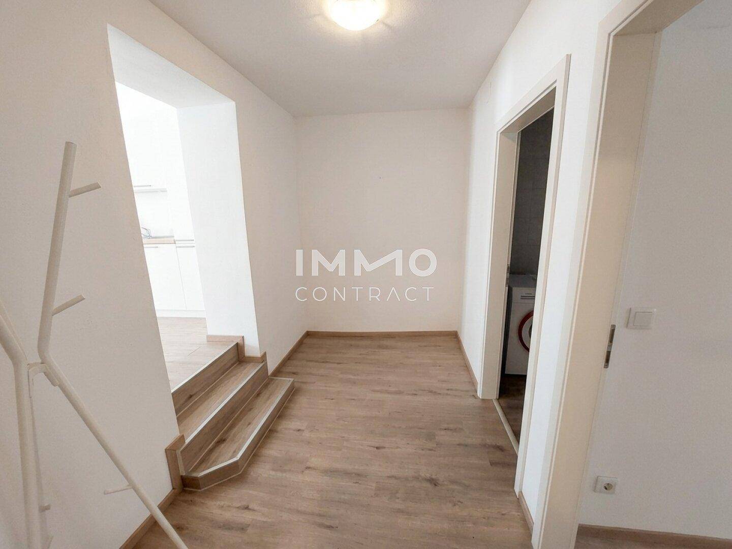 Heller Flur mit Laminatboden, Treppe und Zugang zu einem Hauswirtschaftsraum.