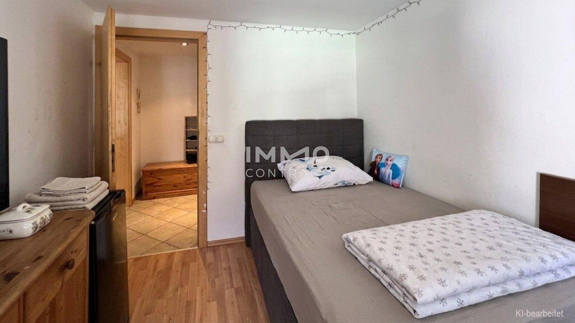 Gemütliches Schlafzimmer mit Einzelbett, Holzboden und Zugang zu einem weiteren Raum.