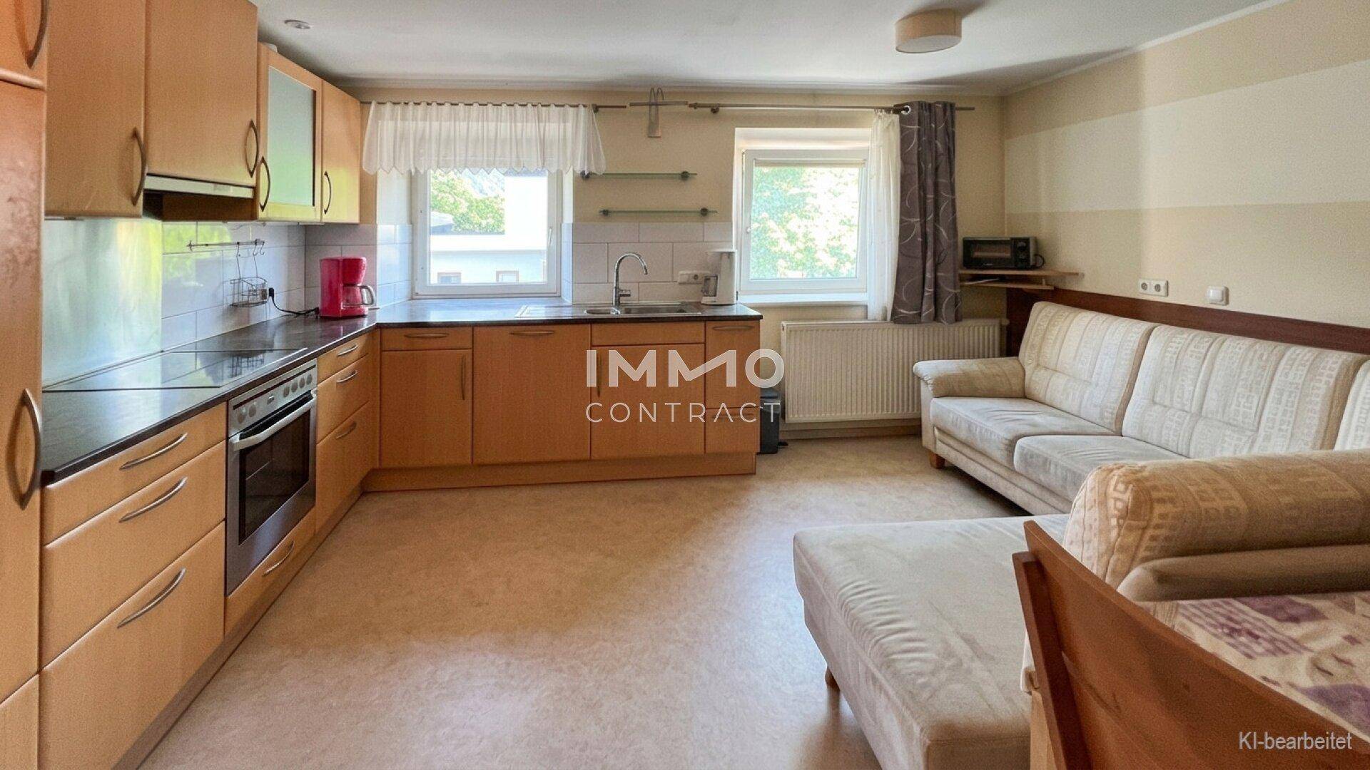 Offener Wohnbereich mit integrierter Küche, Holzschränken und gemütlichem Sofa.