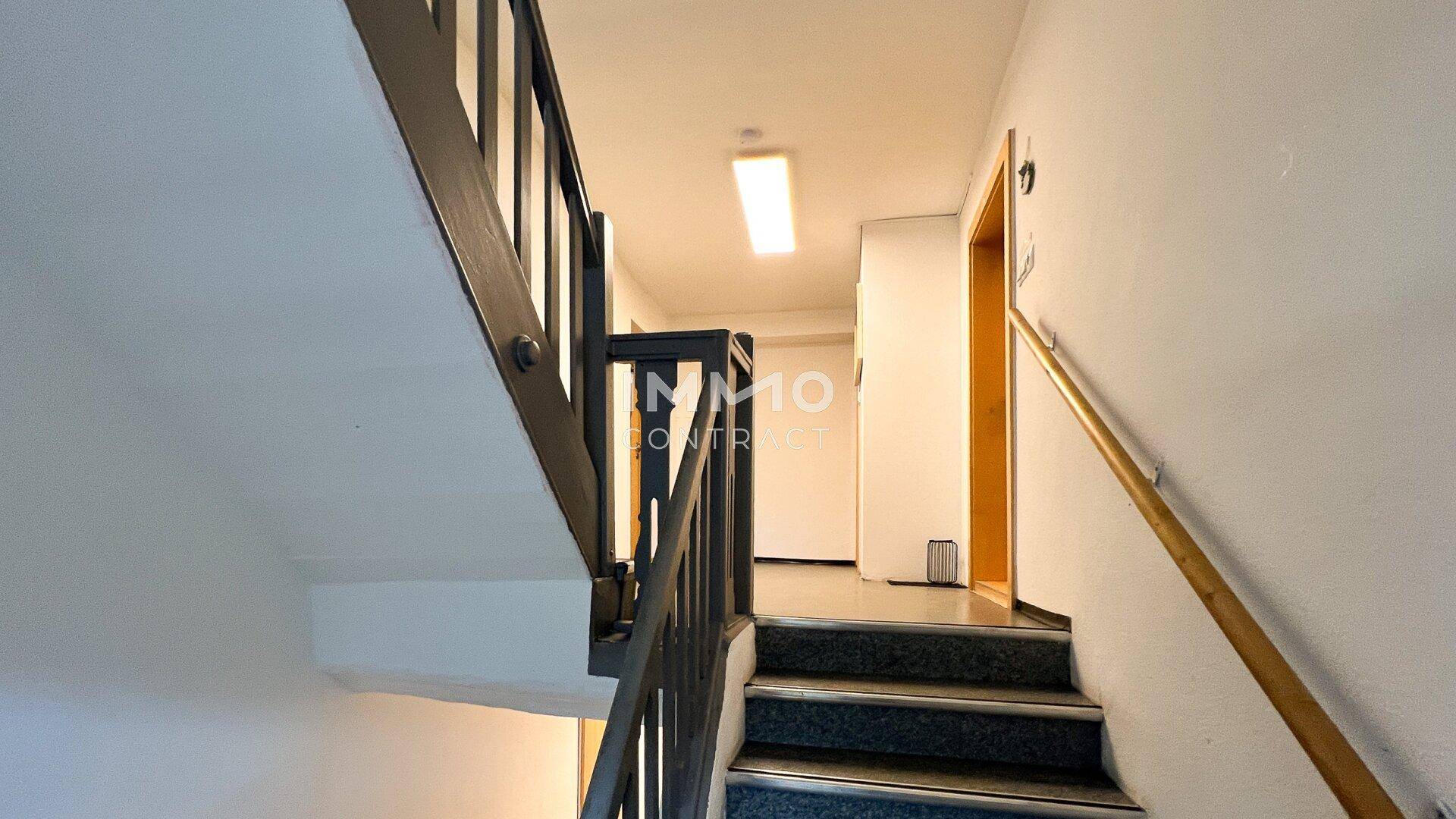 Treppenhaus mit Teppichstufen und Holzgeländer in einem Mehrfamilienhaus.