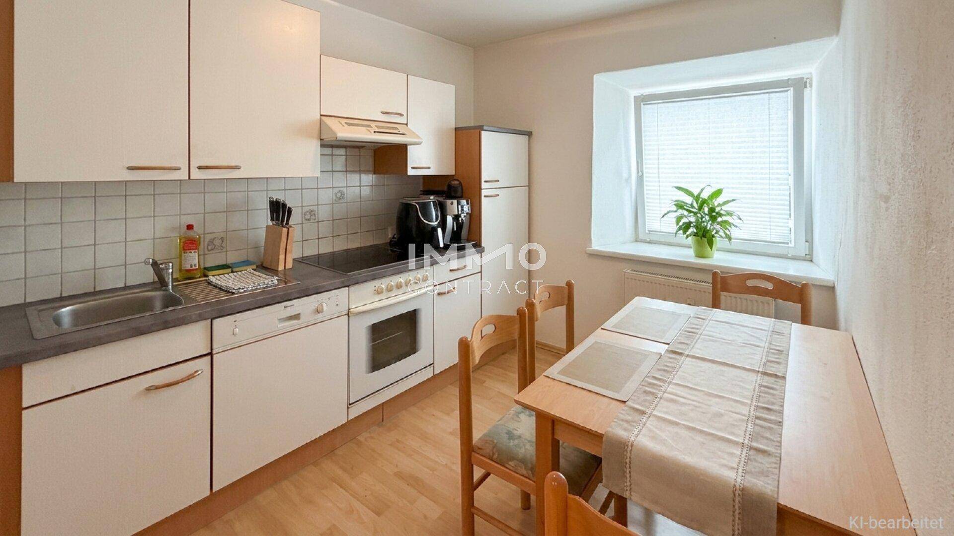 Funktionale Küche mit weißen Schränken, integrierten Geräten und einem Essbereich am Fenster.