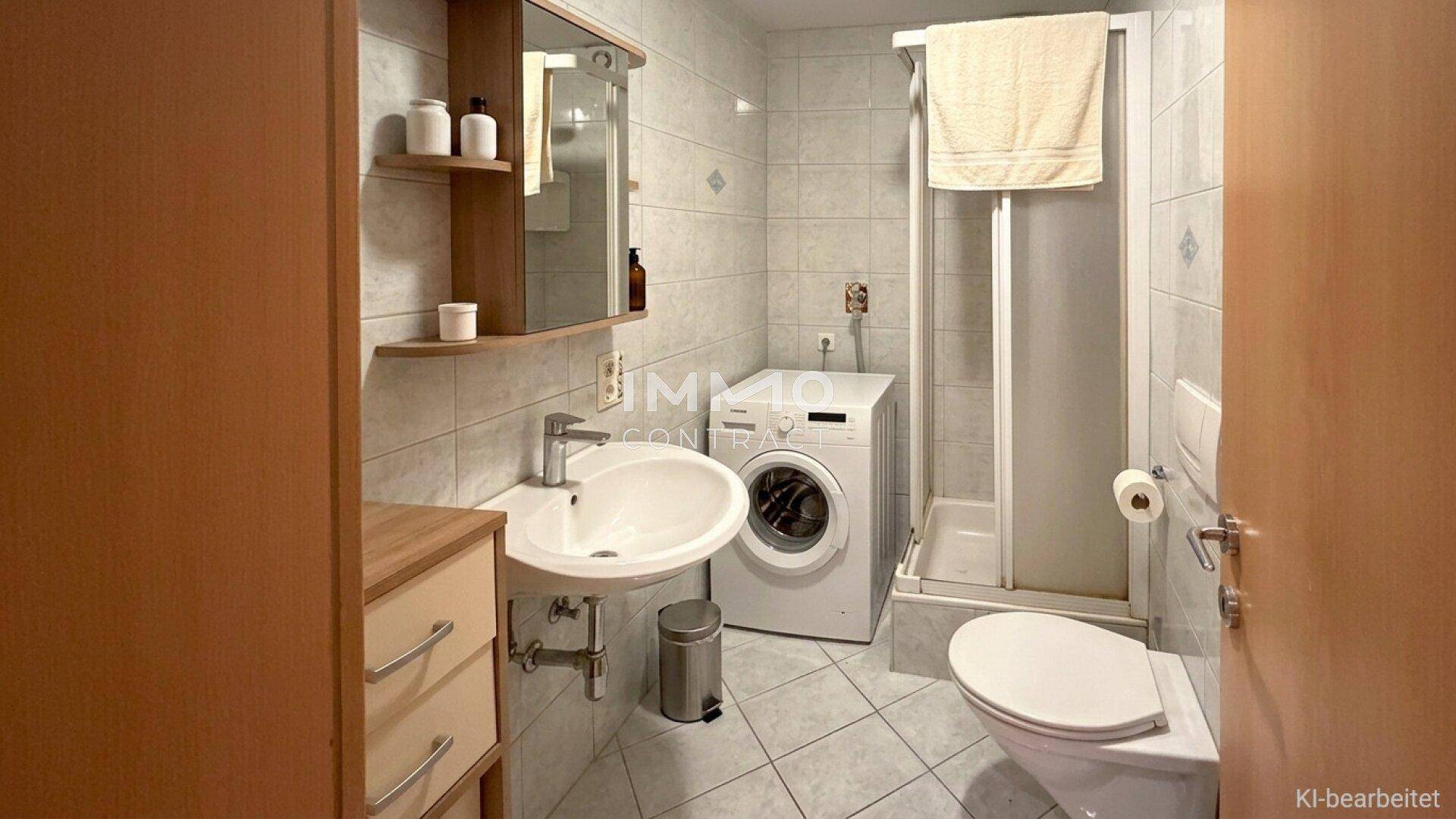 Gefliestes Badezimmer mit Dusche, WC, Waschbecken und integrierter Waschmaschine.