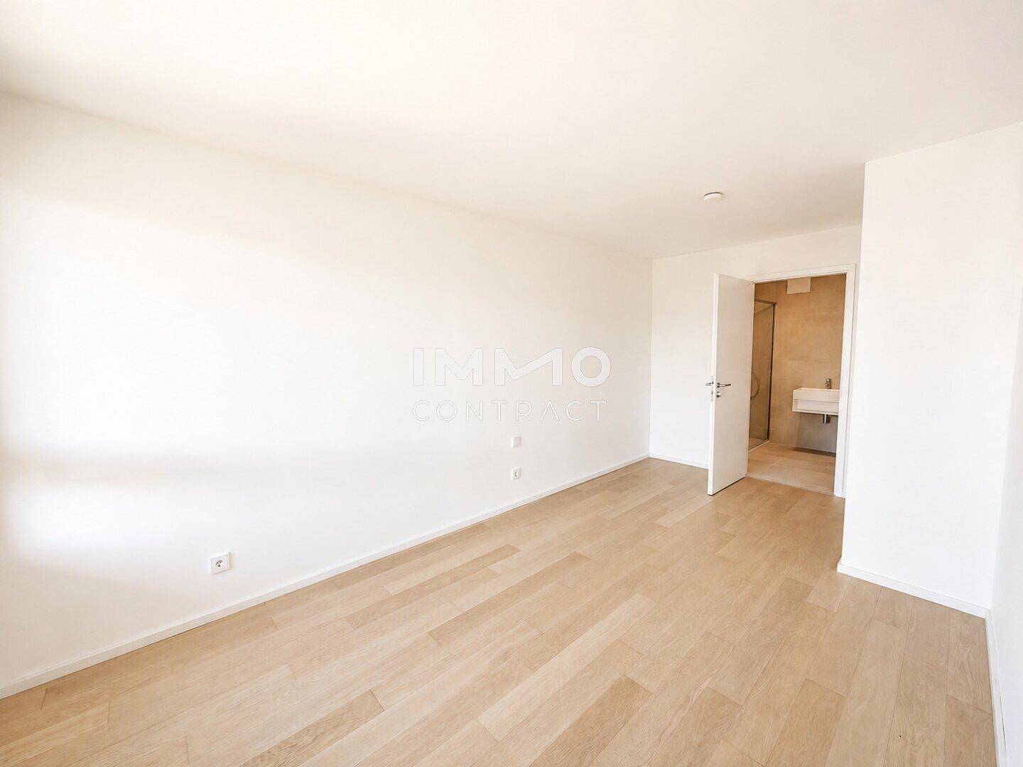 Helles Schlafzimmer mit Holzparkett und direktem Zugang zu einem modernen Badezimmer.