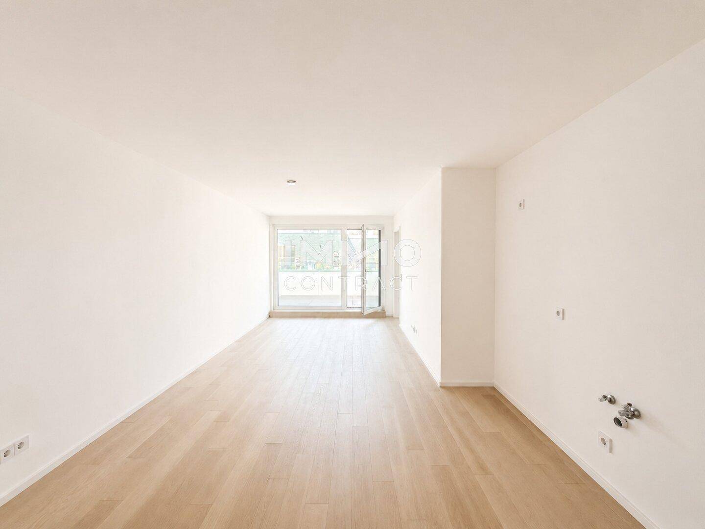 Heller, leerer Wohnraum mit hellem Holzparkett und Zugang zu einem Außenbereich.