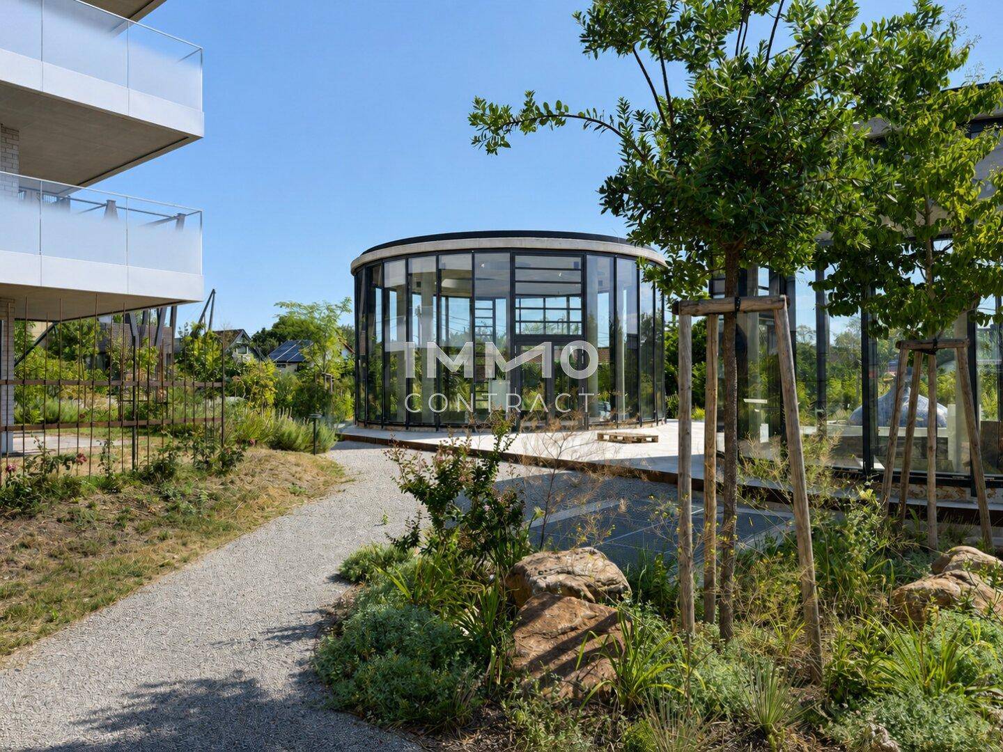Sonniger Gartenbereich mit Kieswegen, üppiger Bepflanzung und moderner Architektur im Hintergrund.