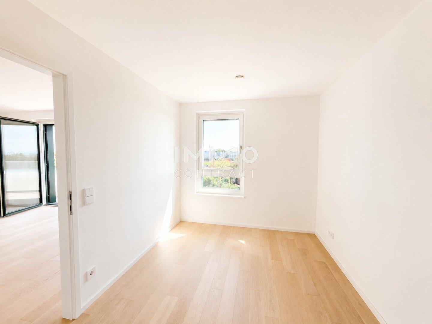 Leeres Zimmer mit hellem Parkettboden und einem Fenster, ideal als Schlaf- oder Arbeitszimmer.