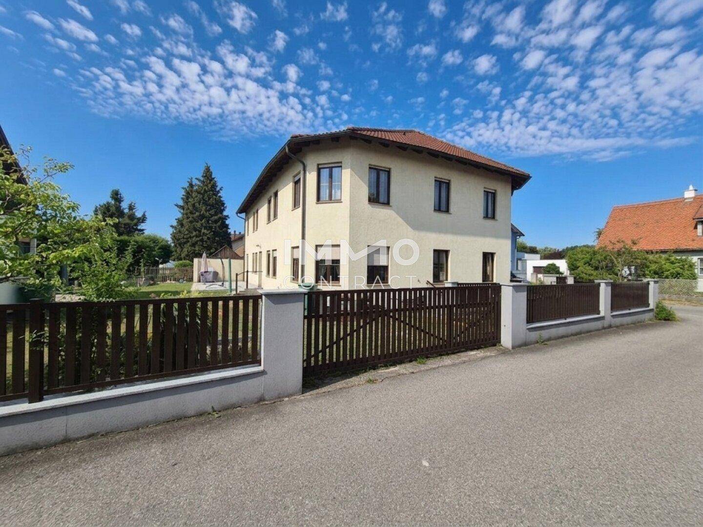 Ansicht des Hauses von der Straße mit einem gepflegten Zaun und einem blauen Himmel.