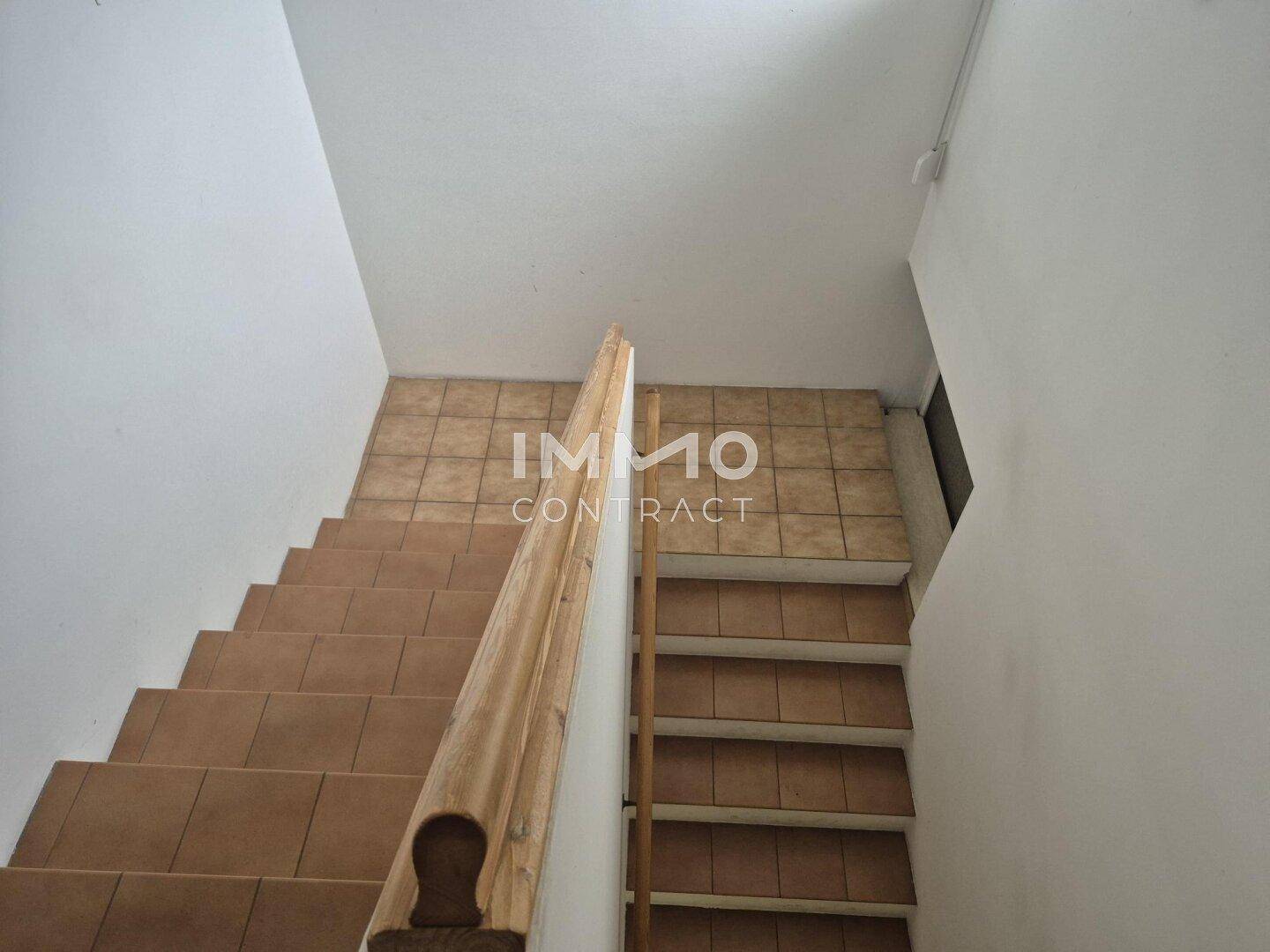 Treppenhaus mit gefliesten Stufen und einem Holzgeländer, das in die obere Etage führt.
