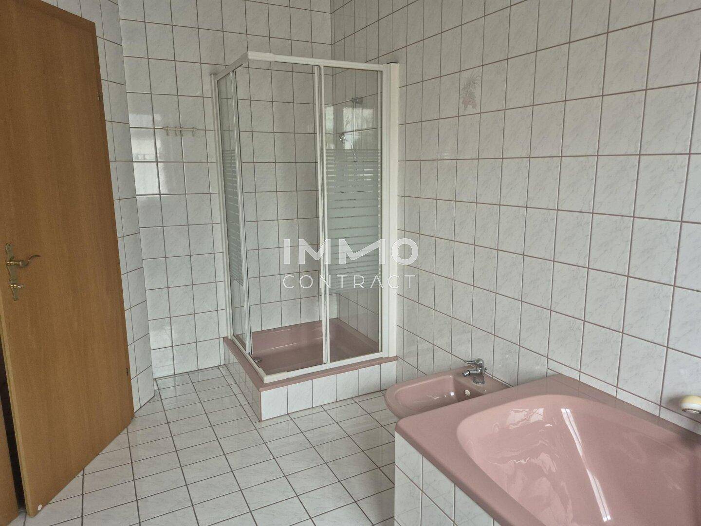 Badezimmer mit weißen Fliesen, Duschkabine, rosa Bidet und passender Badewanne.