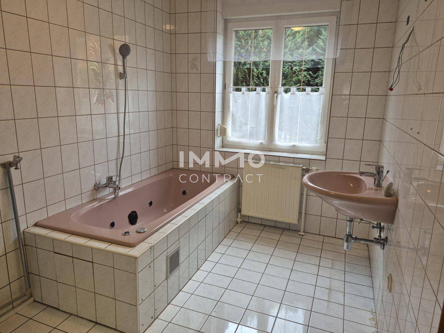 Badezimmer mit weißen Fliesen, einer rosa Badewanne mit Whirlpoolfunktion und Fenster.