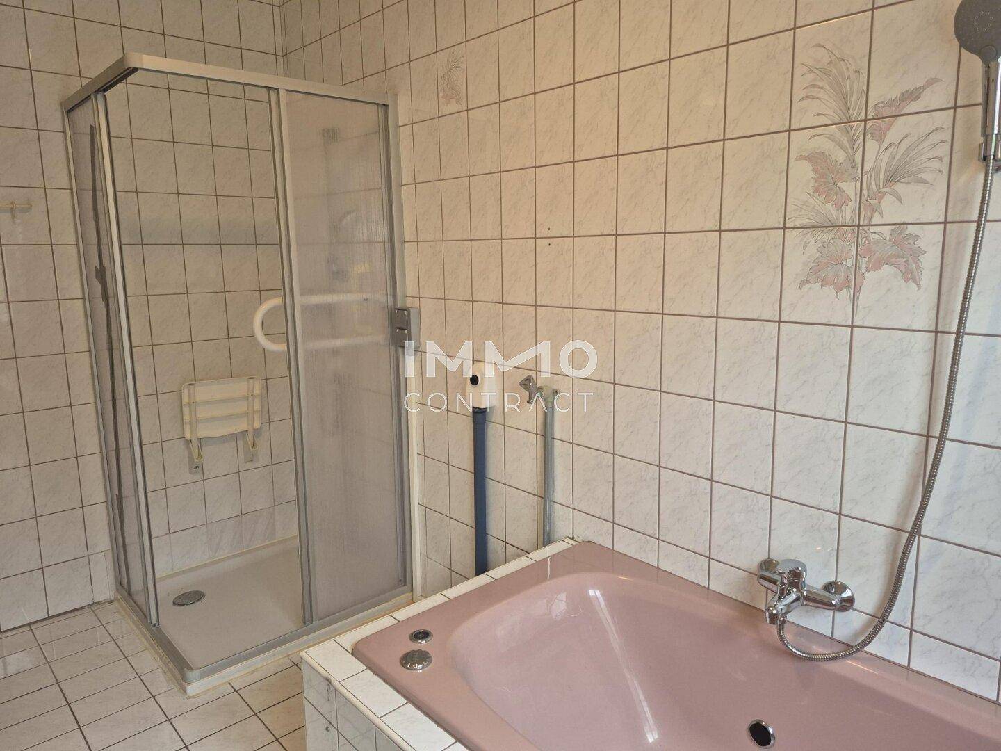 Badezimmer mit weißen Fliesen, einer rosa Badewanne und einer Duschkabine.