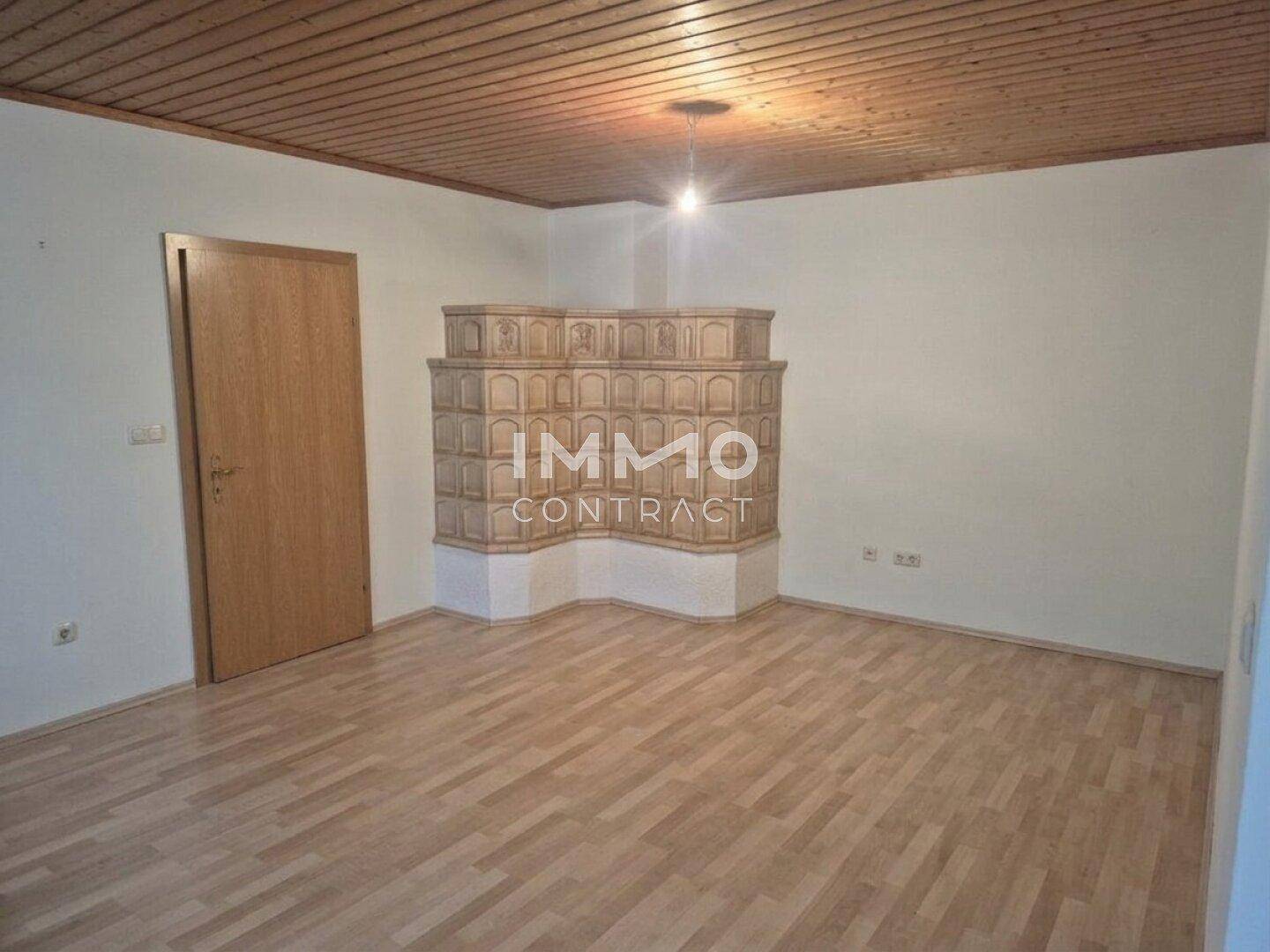 Geräumiger Raum mit Laminatboden, Holzdecke und einem dekorativen Kachelofen als Blickfang.