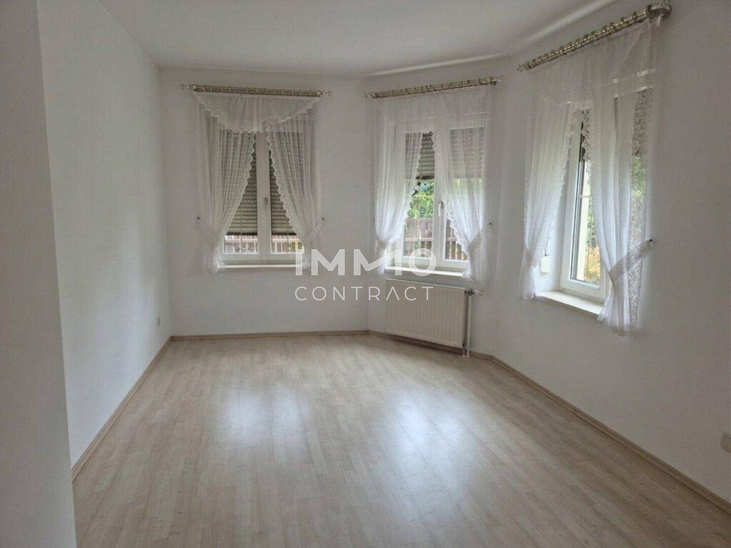 Helles Zimmer mit Laminatboden, Holzdecke und mehreren Fenstern für viel Tageslicht.